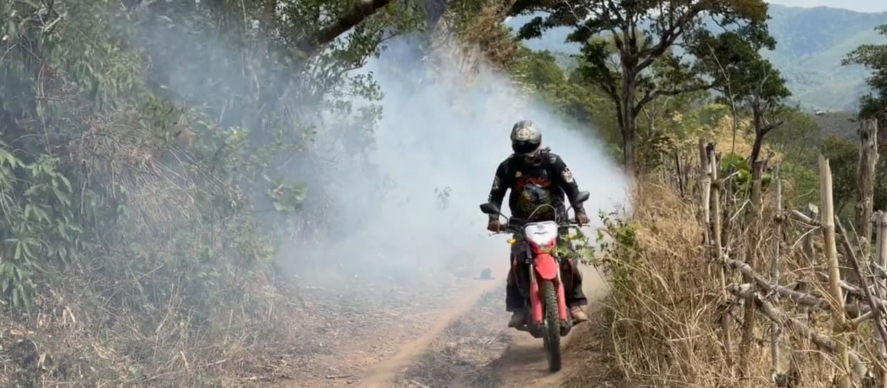 A rider coming out of a cloud of smoke on a dirt track near Mae Sariang
