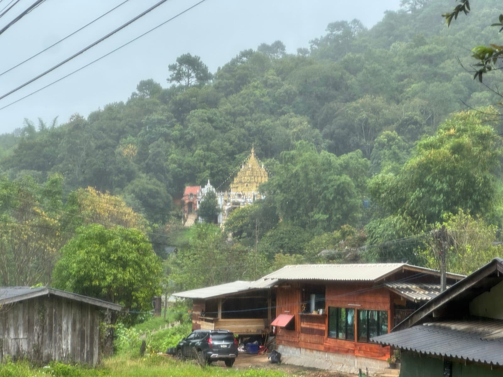 A gold-roofed wat above the village, in the rain.